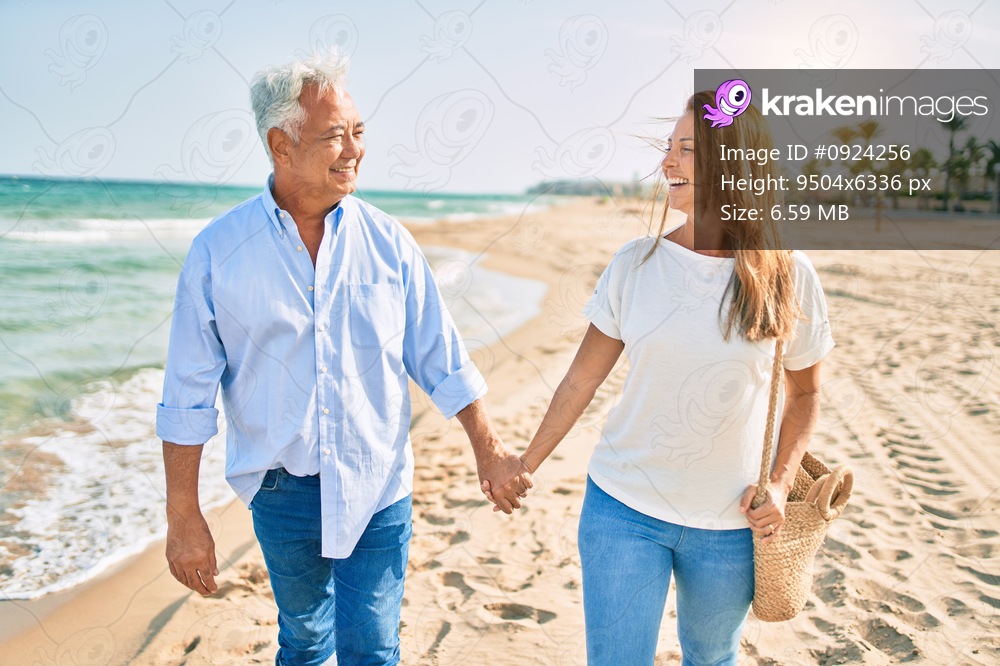 Middle age hispanic couple smiling happy walking at the beach.