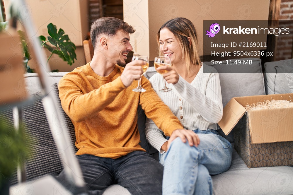 Young man and woman couple toasting with wine sitting on sofa at new home