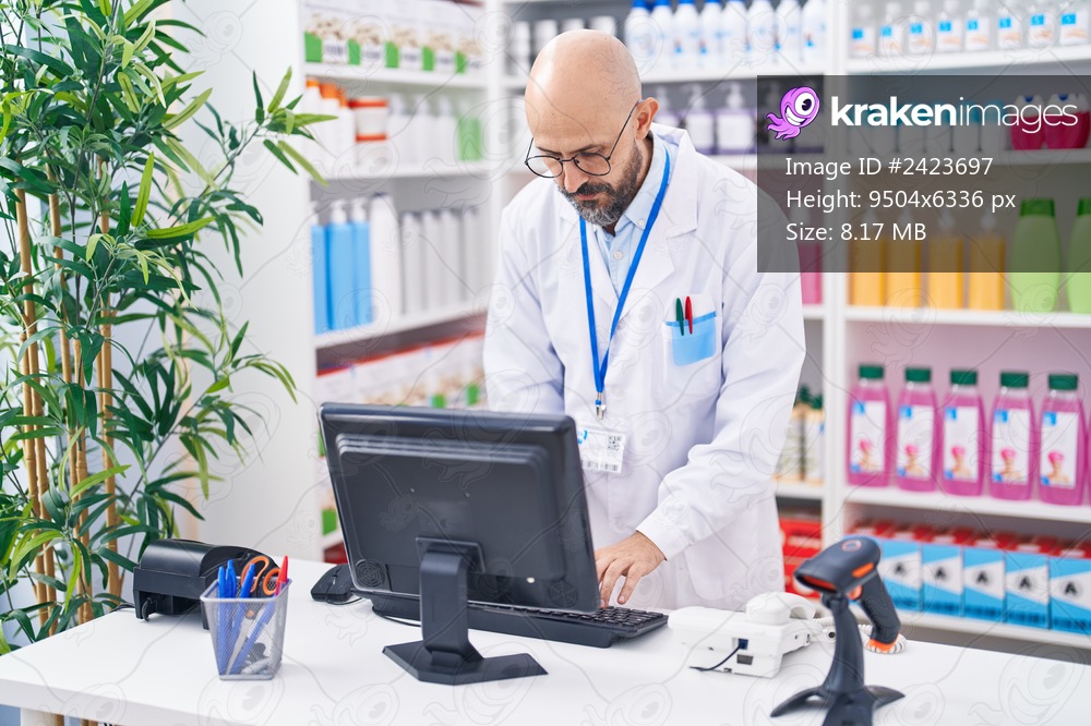 Young bald man pharmacist using computer at pharmacy