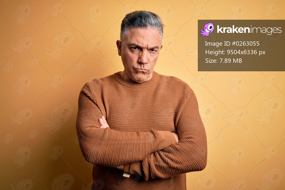 Middle age handsome grey-haired man wearing casual sweater over yellow background skeptic and nervous, disapproving expression on face with crossed arms. Negative person.
