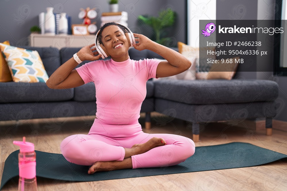 African american woman listening to music sitting on yoga mat at home