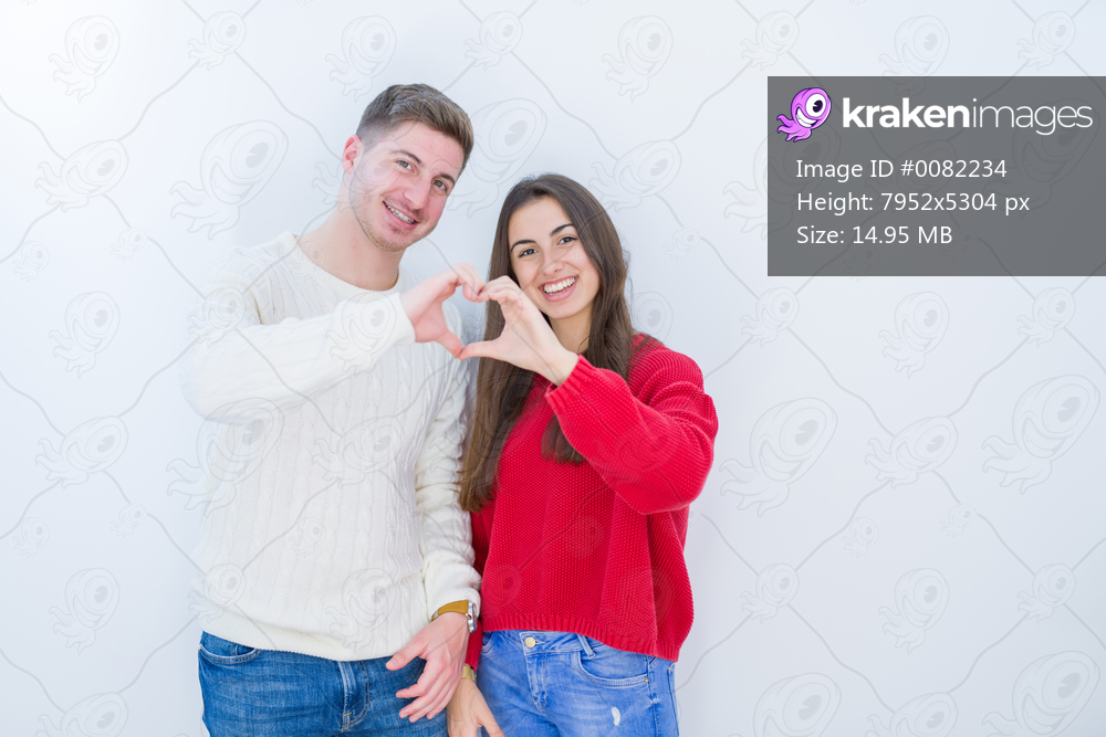 Beautiful young couple over white isolated background smiling in love showing heart symbol and shape with hands. Romantic concept.