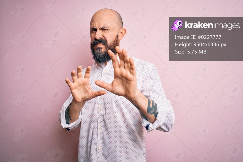 Handsome bald man with beard wearing elegant shirt over isolated pink background disgusted expression, displeased and fearful doing disgust face because aversion reaction. With hands raised