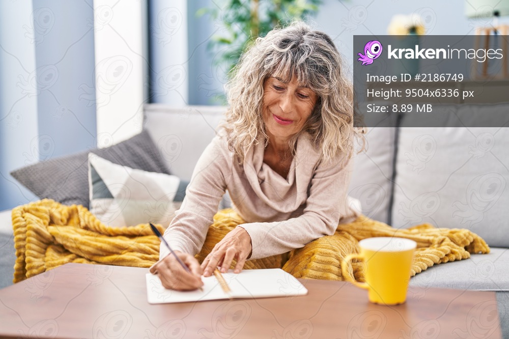 Middle age woman writing on notebook sitting on sofa at home