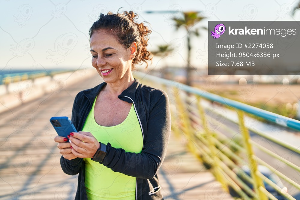 Middle age hispanic woman working out with smartphone at promenade