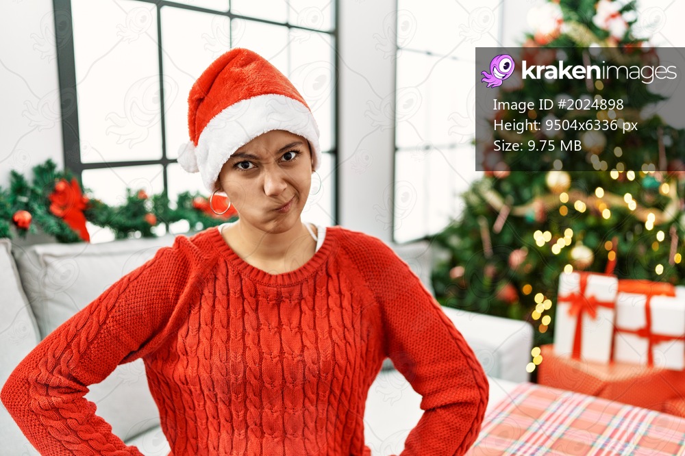 Young hispanic woman with short hair wearing christmas hat sitting on the sofa skeptic and nervous, frowning upset because of problem. negative person. 