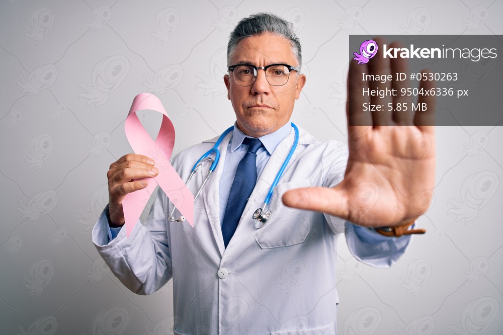 Middle age handsome grey-haired doctor man holding pink cancer ribbon with open hand doing stop sign with serious and confident expression, defense gesture