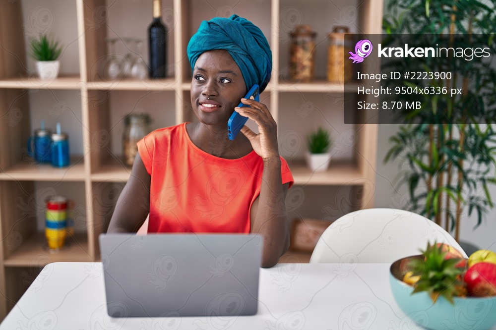 Young african american woman talking on the smartphone using laptop at home