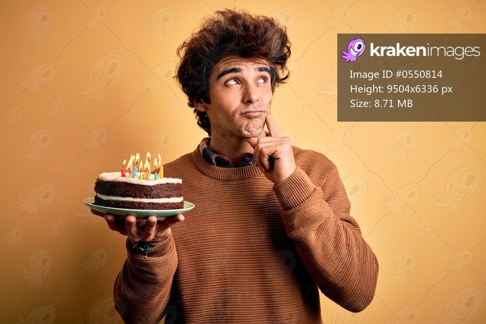 Young handsome man holding birthday cake standing over isolated yellow background serious face thinking about question, very confused idea