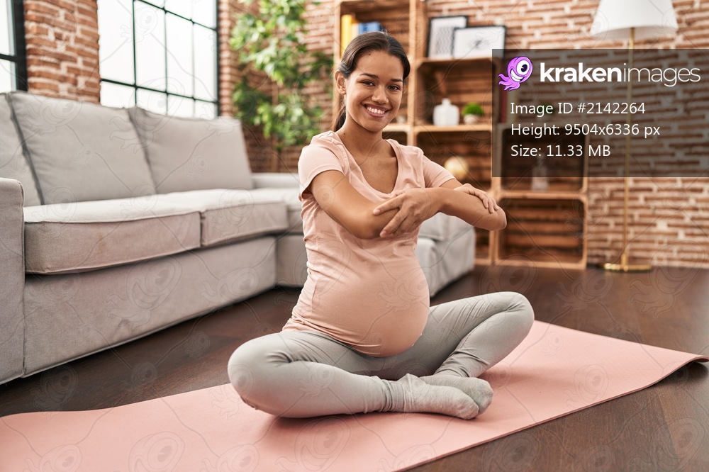 Young latin woman pregnant smiling confident stretching at home