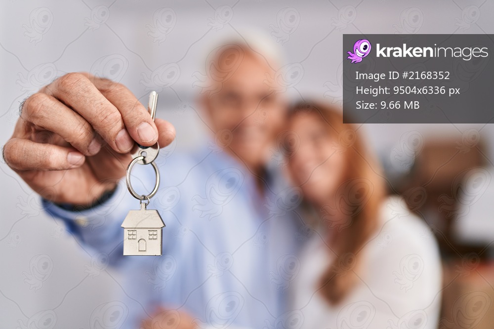 Middle age man and woman couple hugging each other holding key of new house at new home