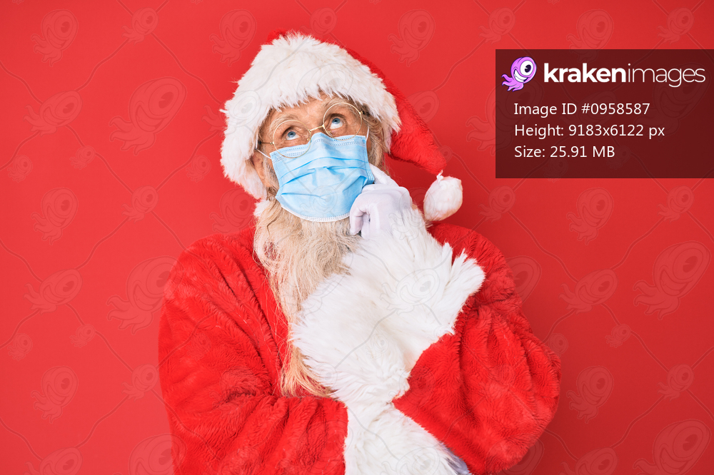 Old senior man wearing santa claus costume wearing safety mask thinking concentrated about doubt with finger on chin and looking up wondering 
