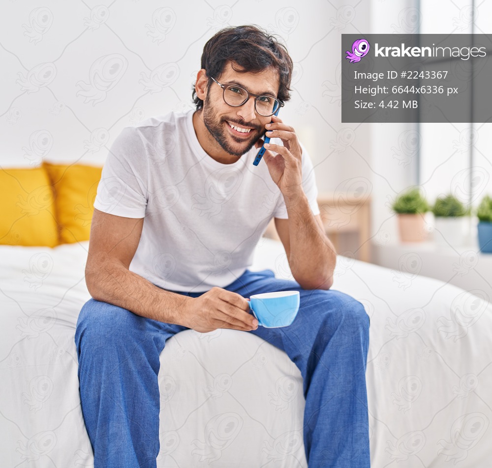 Young hispanic man talking on the smartphone drinking cup of coffee at bedroom