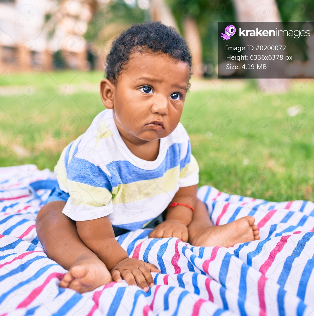 Adorable african american chubby toddler sitting on the grass at the park.
