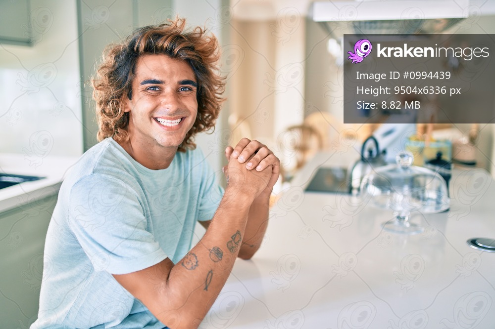 Young hispanic man smiling happy sitting on the table at home