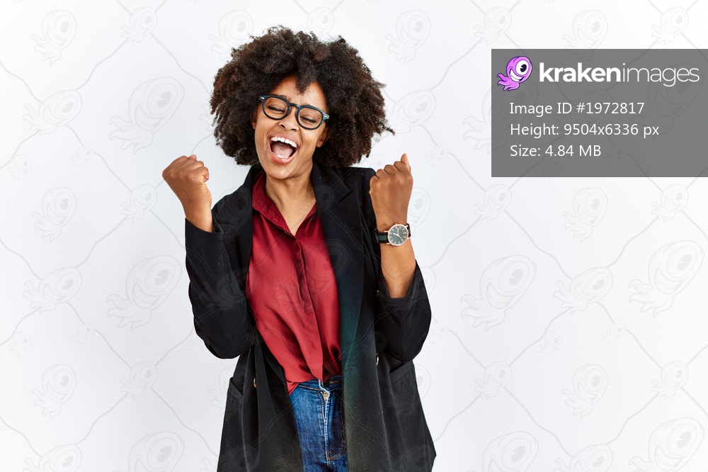 African american woman with afro hair wearing business jacket and glasses celebrating surprised and amazed for success with arms raised and eyes closed. winner concept. 