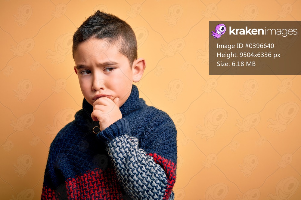 Young little boy kid wearing winter sweater over yellow isolated background with hand on chin thinking about question, pensive expression. Smiling with thoughtful face. Doubt concept.