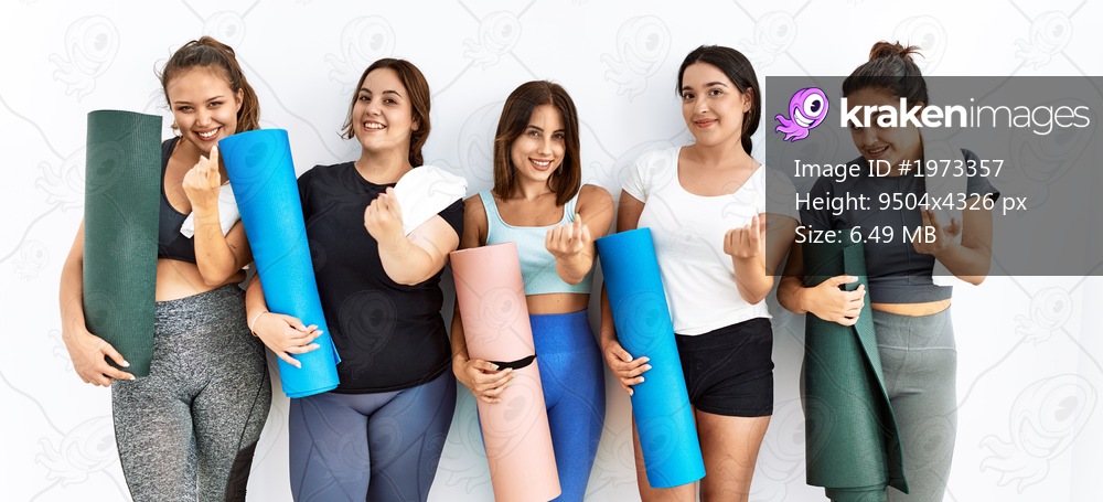 Group of women holding yoga mat standing over isolated background beckoning come here gesture with hand inviting welcoming happy and smiling 