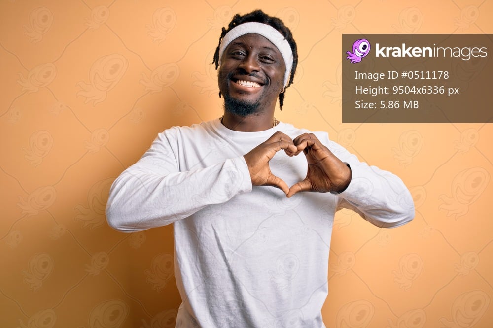 Young african american man doing sport wearing sportswer over isolated yellow background smiling in love showing heart symbol and shape with hands. Romantic concept.