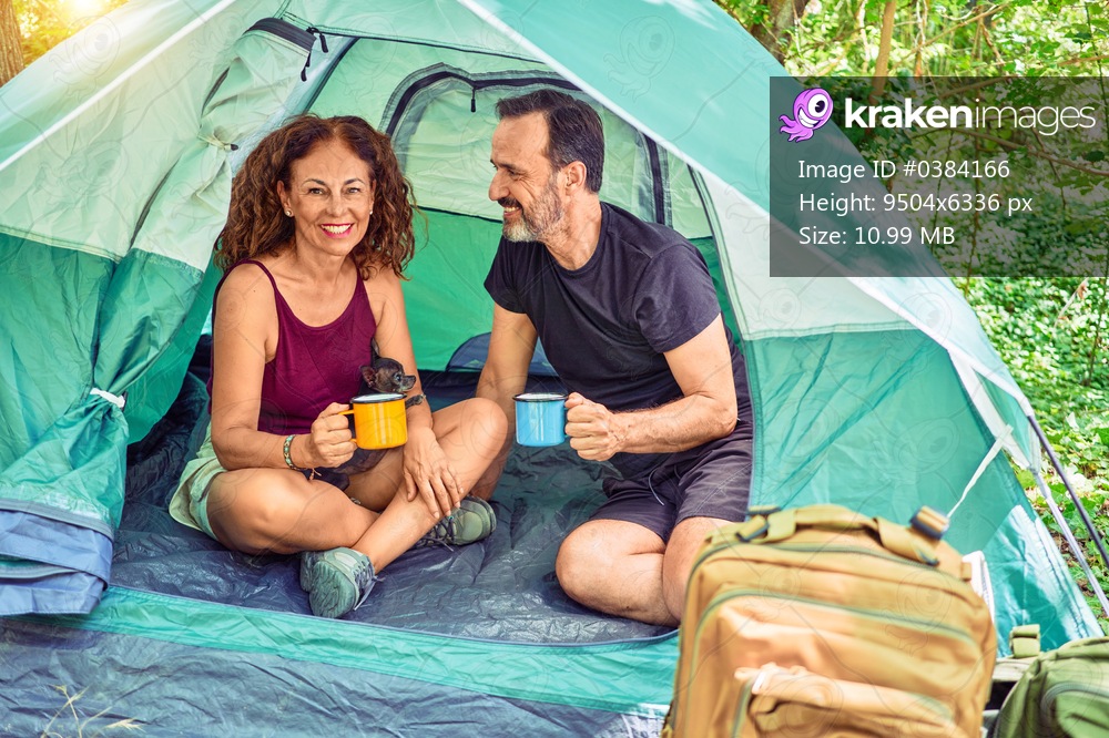 Middle age couple  of hiker smiling happy looking at the camera. Drinking coffee camping at the forest.