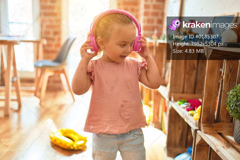 Beautiful blond toddler girl listening to music using headphones at kindergarten