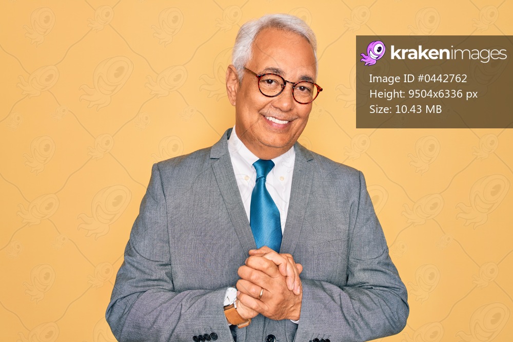 Middle age senior grey-haired handsome business man wearing glasses over yellow background with hands together and crossed fingers smiling relaxed and cheerful. Success and optimistic