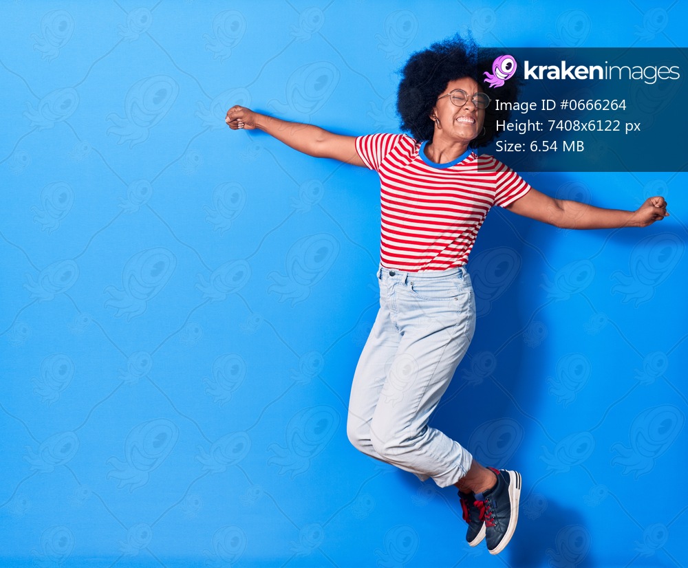 Young beautiful african american woman wearing casual clothes and glasses smiling happy. Jumping with smile on face over isolated blue background