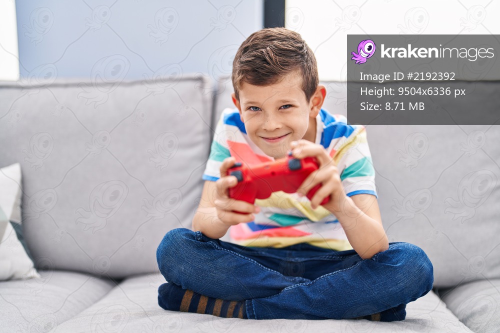Blond child playing video game sitting on sofa at home