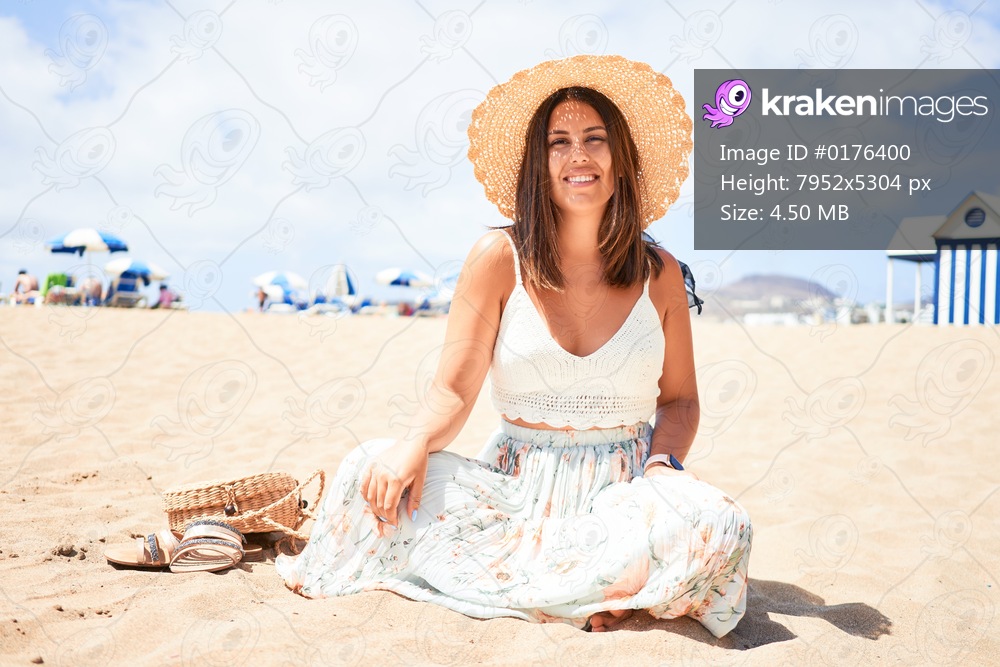 Young beautiful woman smiling happy enjoying summer vacation at the beach sitting on the sun