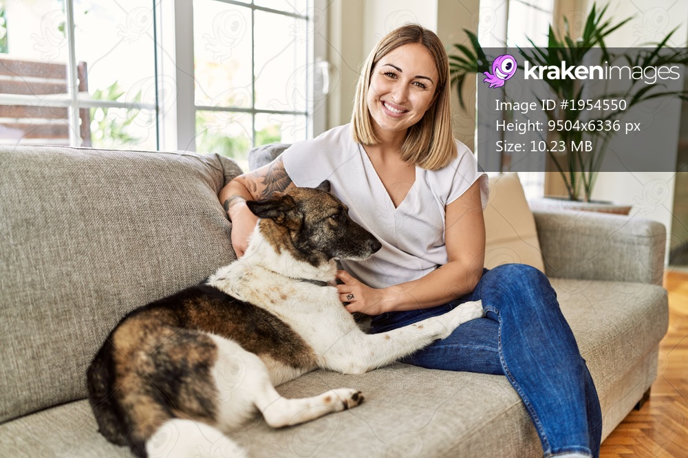 Young caucasian girl smiling happy sitting on the sofa with dog at home.