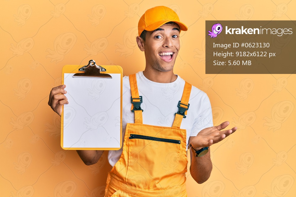 Young handsome african american man wearing courier uniform holding clipboard celebrating achievement with happy smile and winner expression with raised hand 