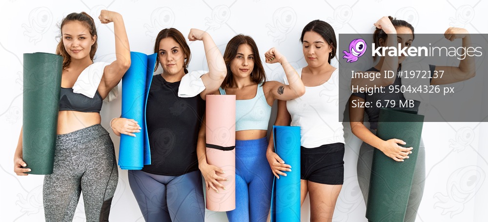 Group of women holding yoga mat standing over isolated background strong person showing arm muscle, confident and proud of power 